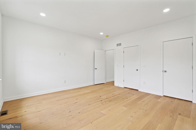 unfurnished bedroom featuring two closets and light wood-type flooring