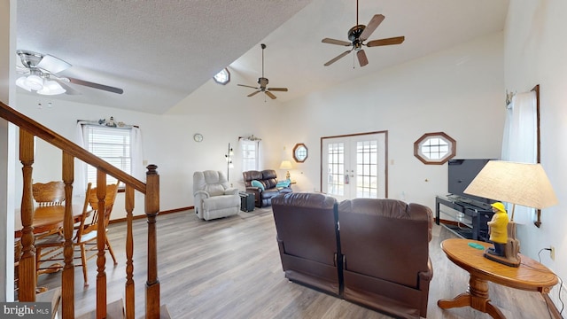 living room featuring vaulted ceiling, light wood-type flooring, a textured ceiling, and french doors