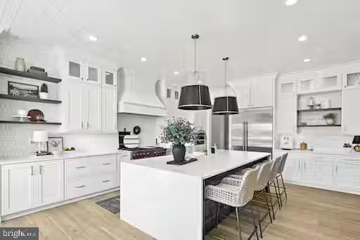 kitchen with premium range hood, a breakfast bar, hanging light fixtures, a kitchen island with sink, and white cabinets