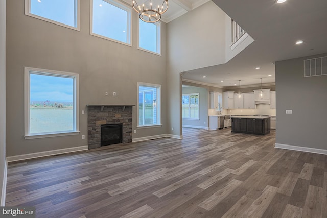 unfurnished living room featuring dark wood-type flooring, a fireplace, crown molding, and an inviting chandelier