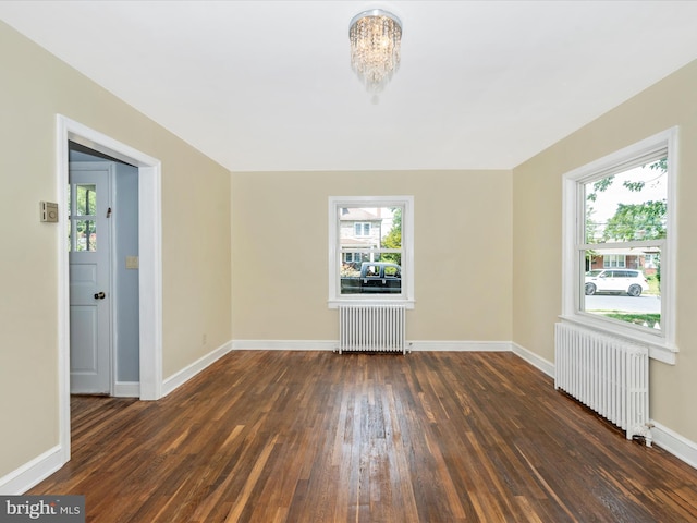 empty room featuring dark hardwood / wood-style floors, radiator, and a notable chandelier