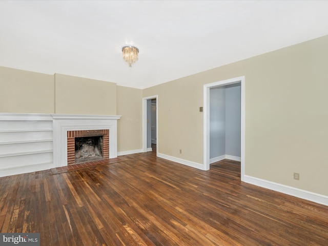 unfurnished living room with built in shelves, a brick fireplace, an inviting chandelier, and dark hardwood / wood-style floors