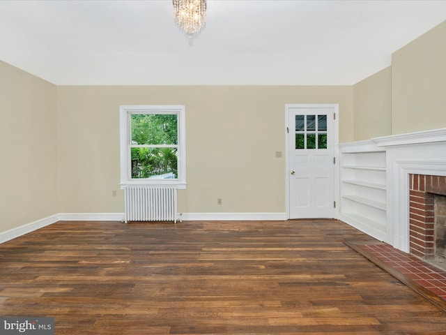 unfurnished living room featuring an inviting chandelier, dark hardwood / wood-style flooring, built in features, a fireplace, and radiator heating unit