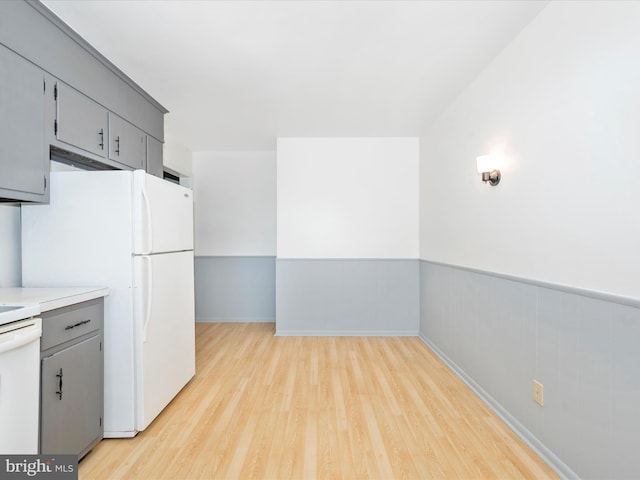 kitchen featuring light wood-type flooring, gray cabinetry, and white appliances