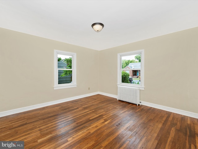 spare room with dark wood-type flooring, a healthy amount of sunlight, and radiator heating unit