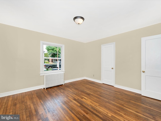 empty room with dark hardwood / wood-style flooring and radiator heating unit