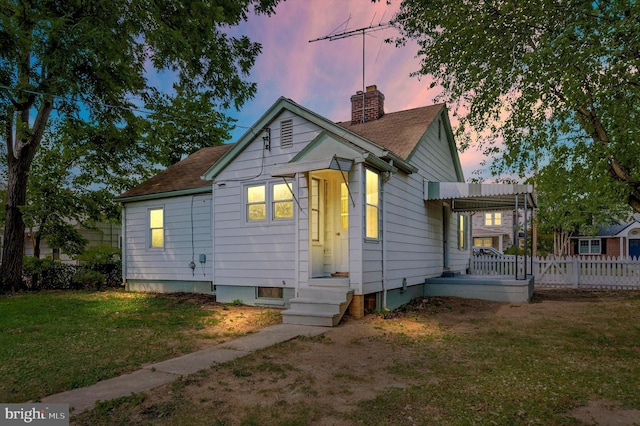 back house at dusk featuring a lawn