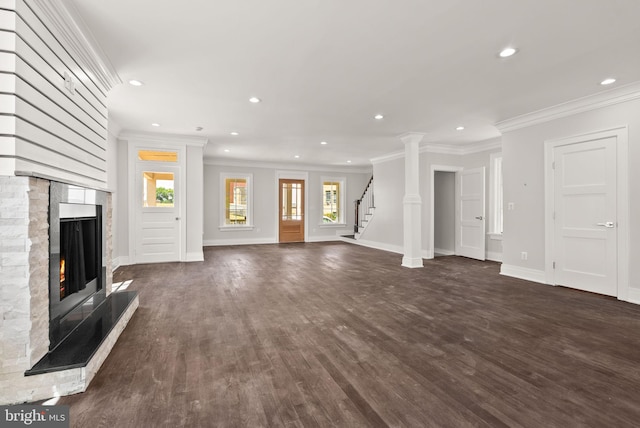 unfurnished living room with ornamental molding, decorative columns, a stone fireplace, and dark wood-type flooring