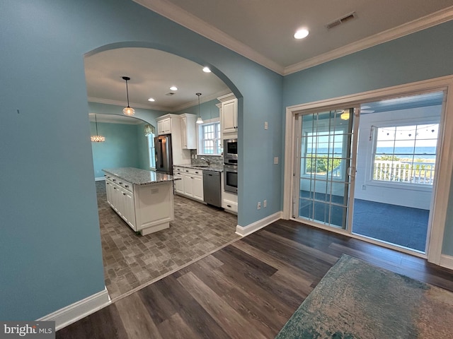 kitchen with stainless steel appliances, dark stone countertops, white cabinets, a center island, and hanging light fixtures