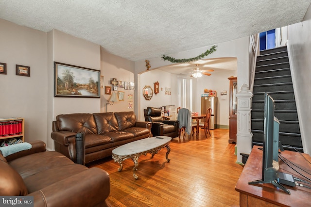 living room with ceiling fan, light hardwood / wood-style flooring, and a textured ceiling