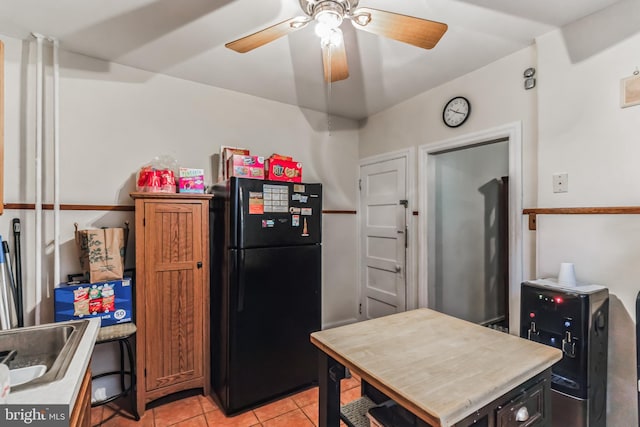 kitchen featuring ceiling fan, black refrigerator, light tile patterned flooring, and sink