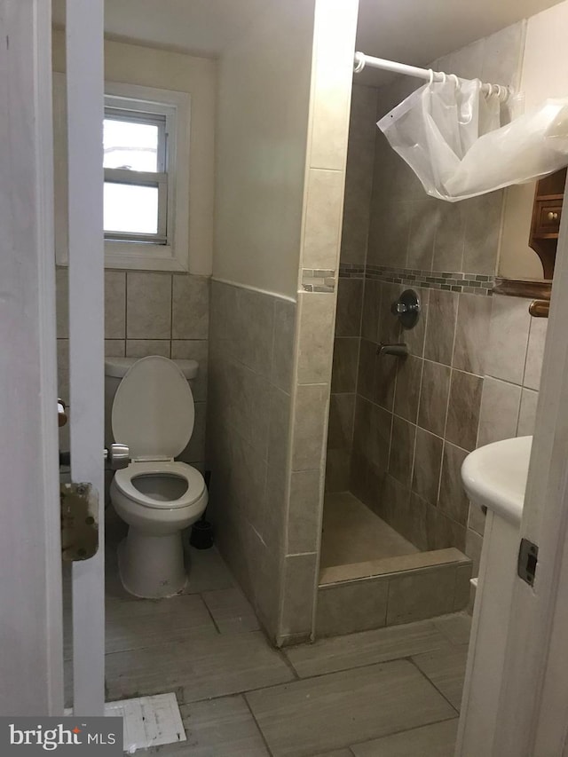 bathroom with a shower with curtain, toilet, and tile walls