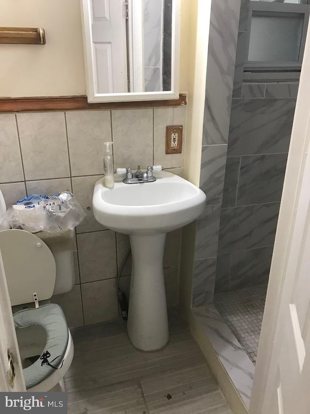 bathroom with a tile shower, toilet, and tile walls