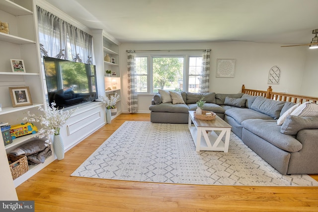 living room featuring ceiling fan, built in shelves, and light hardwood / wood-style flooring