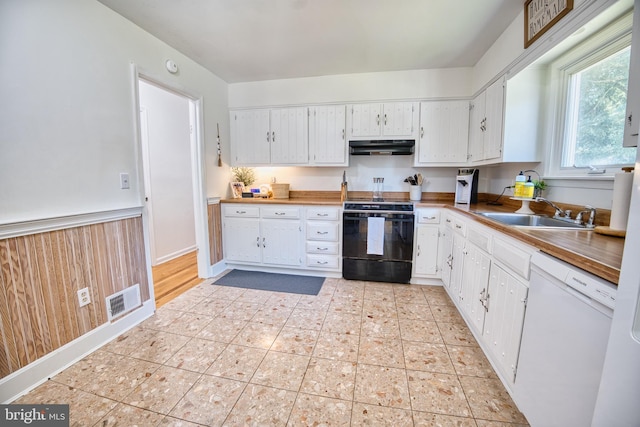 kitchen with white cabinetry, wooden walls, white dishwasher, black range with electric stovetop, and sink