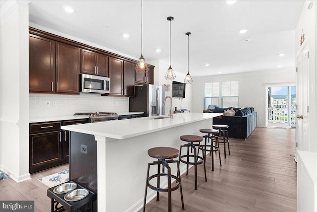 kitchen featuring backsplash, an island with sink, pendant lighting, a breakfast bar, and appliances with stainless steel finishes