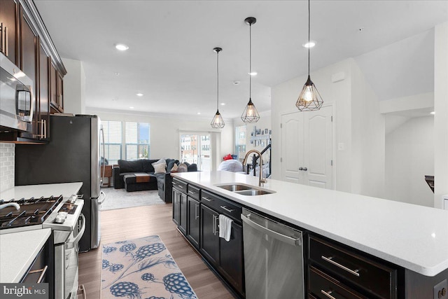 kitchen with appliances with stainless steel finishes, dark brown cabinets, a kitchen island with sink, sink, and decorative light fixtures