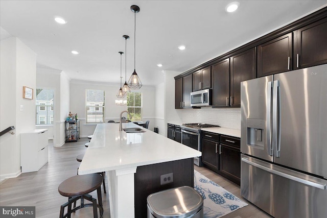 kitchen with sink, a kitchen island with sink, a kitchen breakfast bar, decorative backsplash, and appliances with stainless steel finishes