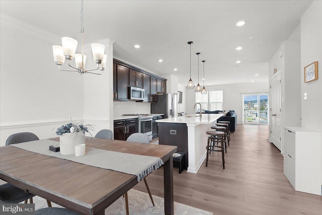 dining space featuring crown molding, light hardwood / wood-style flooring, a notable chandelier, and sink