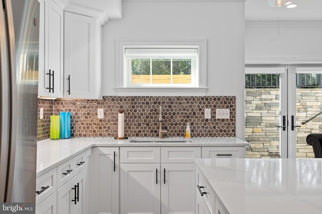 kitchen with stainless steel refrigerator, sink, light stone counters, backsplash, and white cabinets