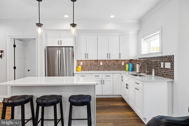 kitchen with pendant lighting, white cabinetry, stainless steel refrigerator, and sink