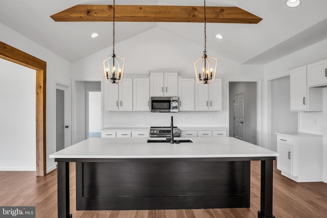 kitchen with stainless steel appliances, lofted ceiling with beams, decorative light fixtures, a center island with sink, and white cabinetry