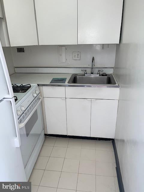 kitchen with white cabinets, light tile patterned floors, sink, and white appliances