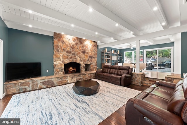 living room featuring a stone fireplace, beam ceiling, dark wood-type flooring, and ceiling fan