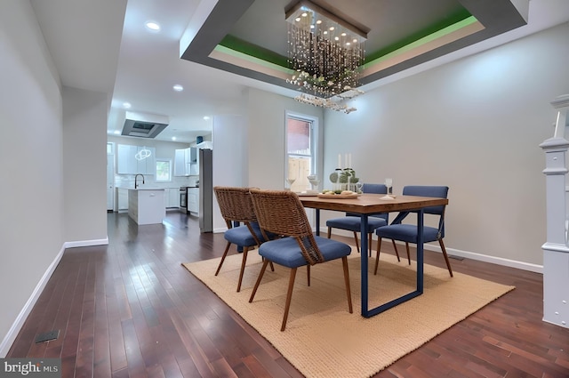 dining room featuring dark hardwood / wood-style floors, a raised ceiling, a notable chandelier, and sink