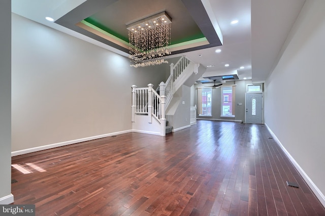 unfurnished living room with ceiling fan with notable chandelier, dark hardwood / wood-style floors, and a raised ceiling