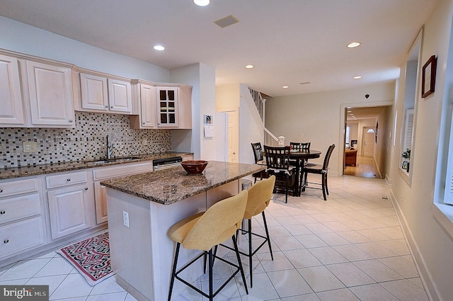 kitchen featuring dark stone counters, sink, light tile patterned floors, a center island, and a breakfast bar area