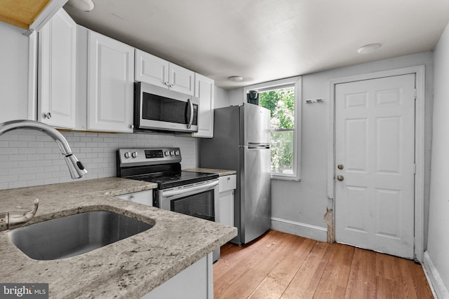 kitchen with appliances with stainless steel finishes, tasteful backsplash, light stone counters, sink, and white cabinets