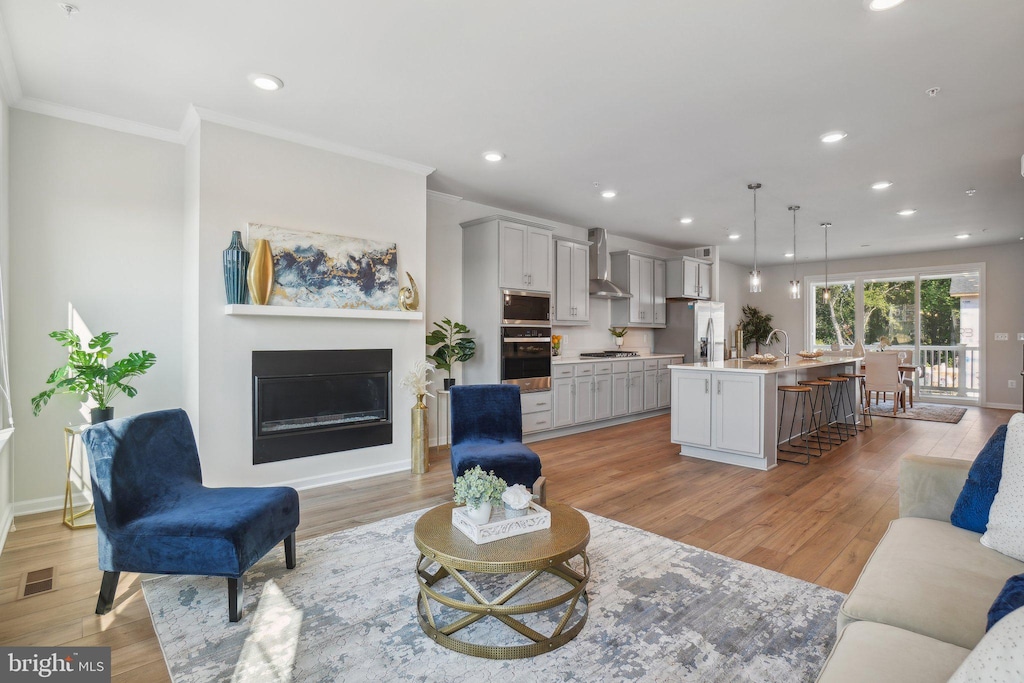 living room featuring crown molding, recessed lighting, visible vents, light wood-style flooring, and a glass covered fireplace