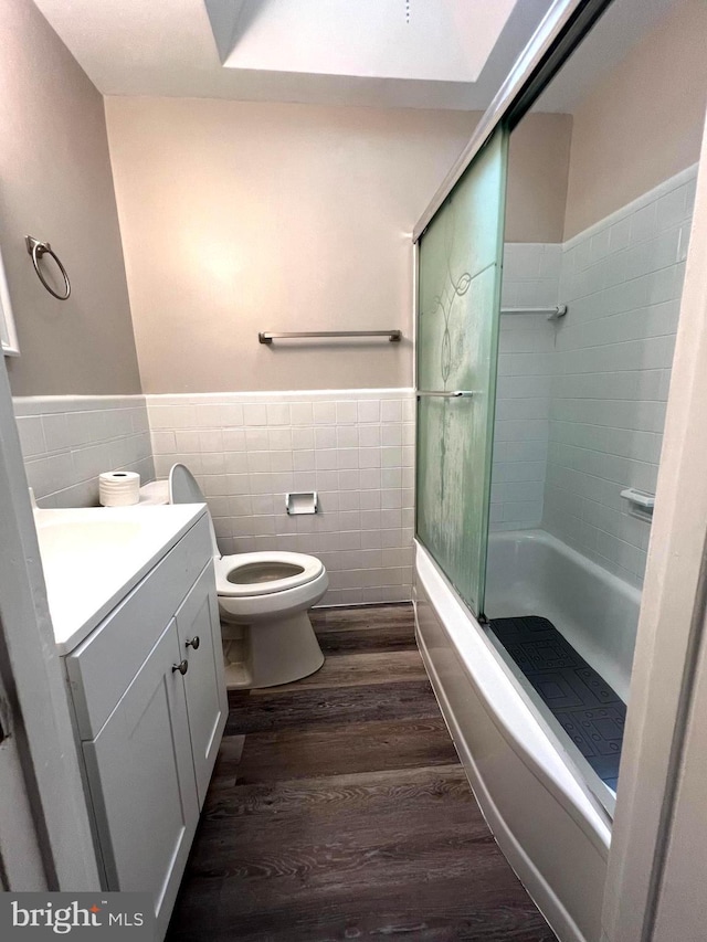 full bathroom with vanity, shower / bath combination with glass door, tile walls, hardwood / wood-style floors, and toilet