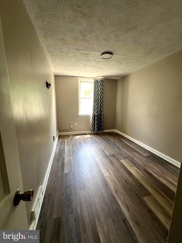 unfurnished room featuring a textured ceiling and dark hardwood / wood-style floors