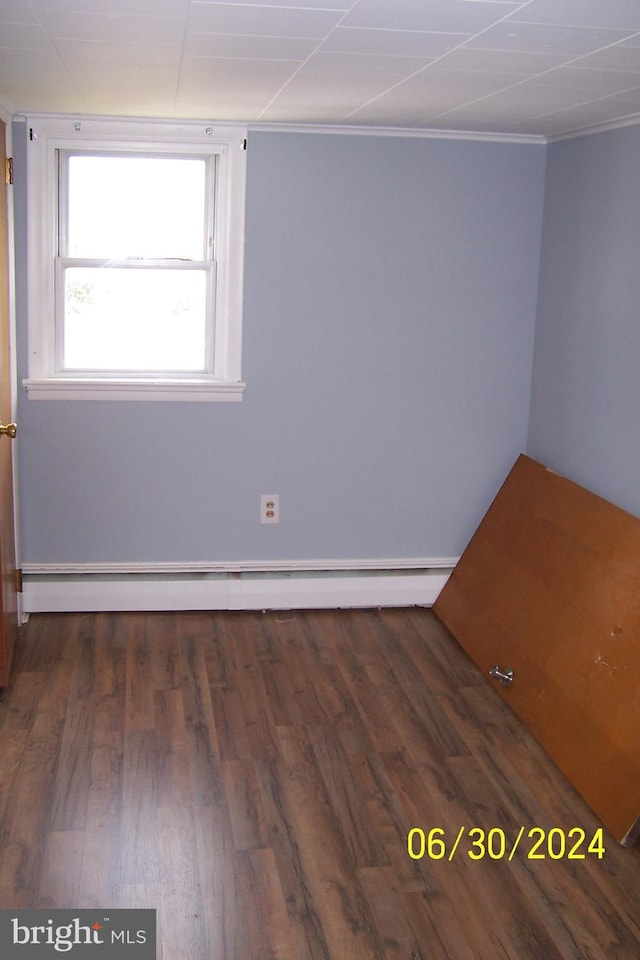 spare room featuring crown molding, baseboard heating, and dark wood-type flooring