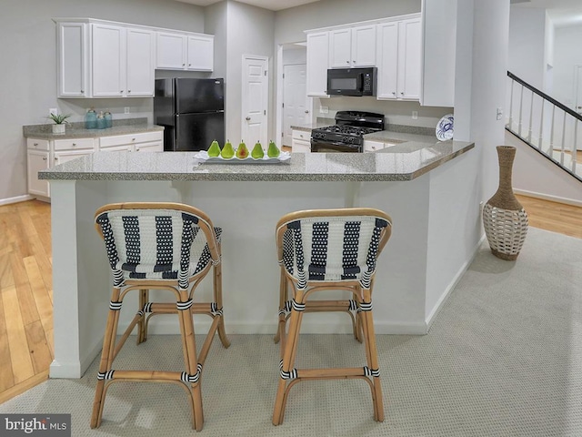 kitchen with kitchen peninsula, white cabinetry, and black appliances