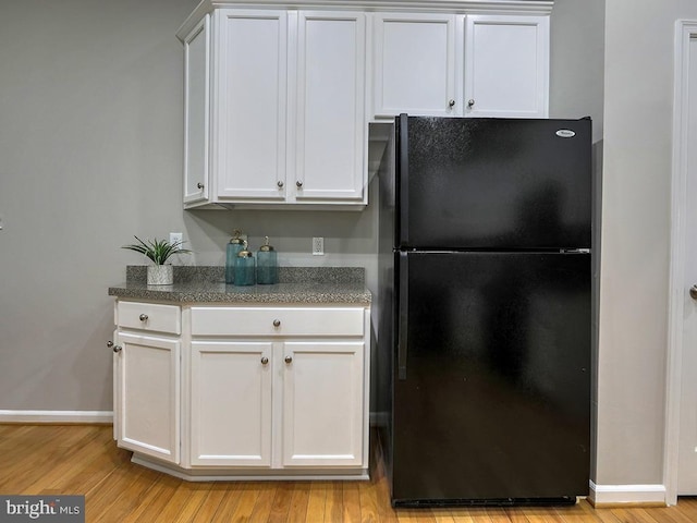 kitchen featuring white cabinetry, black fridge, and light wood-type flooring