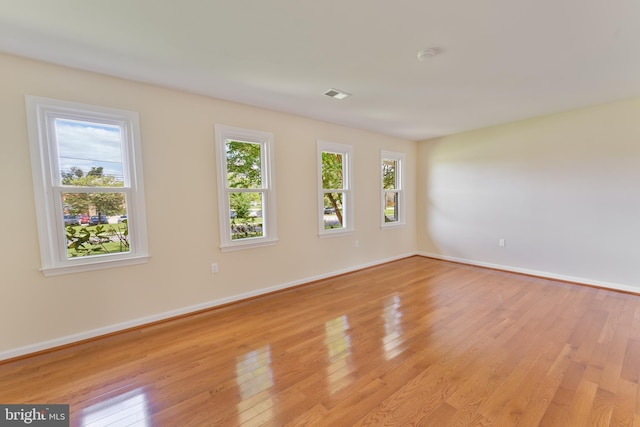 unfurnished room with visible vents, light wood finished floors, a wealth of natural light, and baseboards