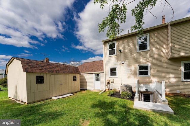 rear view of property with a storage shed, a yard, central AC, and an outbuilding