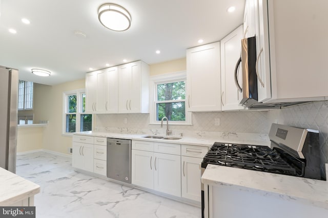 kitchen with white cabinets, appliances with stainless steel finishes, light stone counters, marble finish floor, and a sink