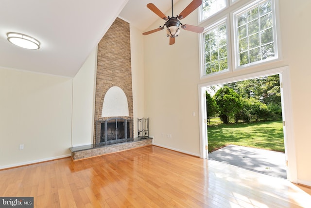 unfurnished living room featuring plenty of natural light, high vaulted ceiling, a fireplace, and wood-type flooring