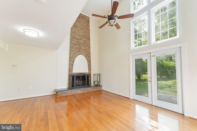 unfurnished living room with a brick fireplace, baseboards, light wood-style flooring, and a towering ceiling