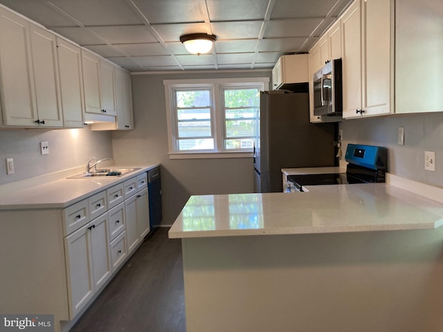 kitchen featuring kitchen peninsula, light stone counters, sink, black appliances, and white cabinetry