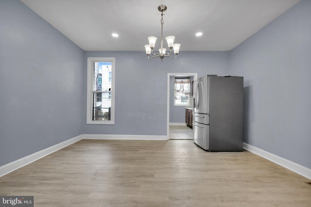 unfurnished dining area with a notable chandelier and light wood-type flooring