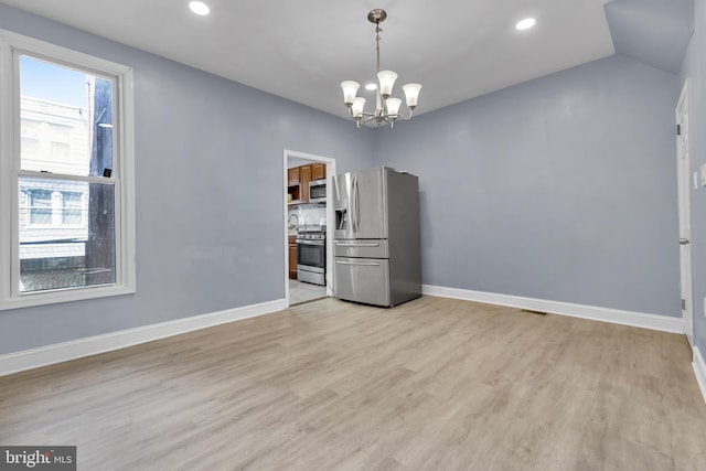 spare room featuring light hardwood / wood-style floors, vaulted ceiling, and a notable chandelier