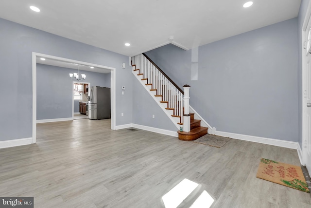 unfurnished living room with light wood-type flooring and an inviting chandelier