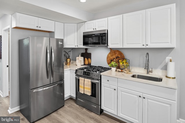 kitchen with sink, white cabinets, stainless steel appliances, and light hardwood / wood-style floors