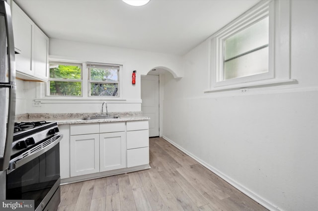 kitchen with sink, light hardwood / wood-style floors, gas stove, and white cabinets