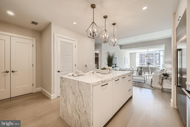 kitchen with pendant lighting, a center island, light stone countertops, light hardwood / wood-style floors, and white cabinetry